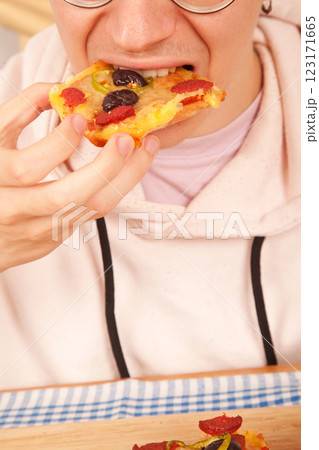 Bearded Caucasian white young male wearing pink t-shirt eating delicious pizza slices on bamboo cutting board on table Bearded Caucasian white young male wearing pink t-shirt eating delicious pizza slices on bamboo cutting board on table 123171665