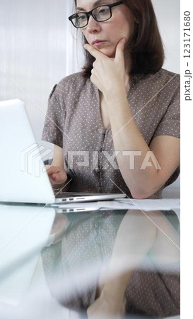 Focused businesswoman in brawn dotted blouse is using laptop and thinking with hand on chin, working on a project in a bright office. Business people concept Focused businesswoman in brawn dotted blouse is using laptop and thinking with hand on chin, working on a project in a bright office. Business people concept 123171680