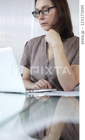 Focused businesswoman in brawn dotted blouse is using laptop and thinking with hand on chin, working on a project in a bright office. Business people concept Focused businesswoman in brawn dotted blouse is using laptop and thinking with hand on chin, working on a project in a bright office. Business people concept 123171695