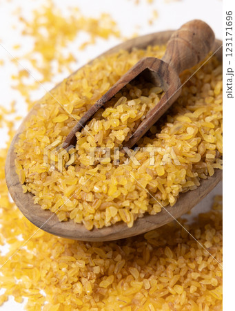 Raw dry uncooked yellow bulgur grain in a wooden spoon on a bowl closeup. Ancient food 123171696