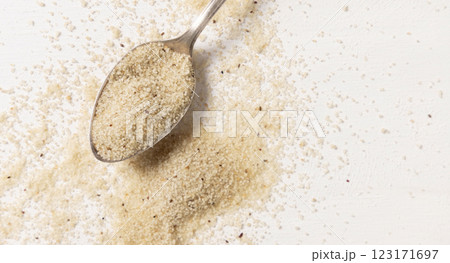 Raw uncooked fonio seeds in a metal spoon on white table, top view. African ancient pseudocereal 123171697