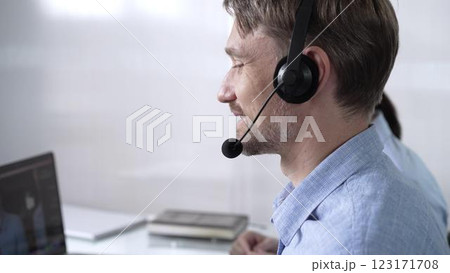 Focused male call center operator in blue casual shirt is assisting clients online, providing customer support and answering inquiries. Call center 123171708