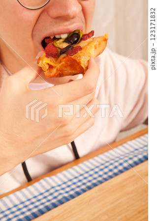 Bearded Caucasian white young male wearing pink t-shirt eating delicious pizza slices on bamboo cutting board on table Bearded Caucasian white young male wearing pink t-shirt eating delicious pizza slices on bamboo cutting board on table 123171832