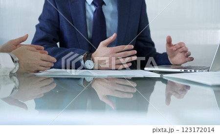 Business partners or lawyers dressed in blue are reviewing and discussing contract papers during a meeting, using a laptop and documents on a glass table. Businesspeople 123172014