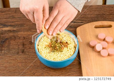 A young woman pours dried herbs from a saucer onto instant noodles. 123172749