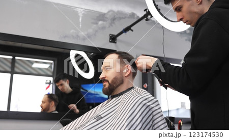 Professional barber concentrating while skillfully using clippers to cut and style a male customer's hair in a modern barbershop, creating a trendy and polished look 123174530