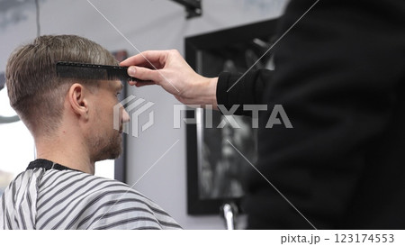 Barber carefully combing hair, client wearing protective cape, preparing for precision styling inside sleek contemporary barbershop setting 123174553