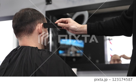 Professional hairdresser styling male client's hair, mirror reflecting classic barber pole, salon interior with modern grooming ambiance 123174587