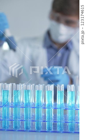 Test tubes with a blue liquid, close-up view. Scientist holding pipette conducting experiments in laboratory on the background. Science and Medicine 123174615