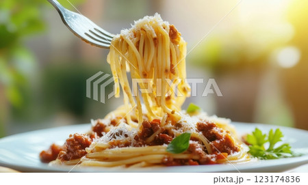 A fork lifts spaghetti Bolognese mid-air, with glistening sauce and falling Parmesan. Warm natural light and a sunlit window create a fresh, inviting Italian home-cooked atmosphere. 123174836