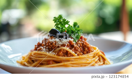 Elegant spaghetti Bolognese plated with rich tomato sauce, fresh parsley, olives, and Parmesan, bathed in soft natural light near a sunlit window, evoking a cozy, inviting Italian dining experience. 123174854