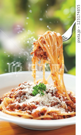 A fork lifts spaghetti Bolognese mid-air, with glistening sauce and falling Parmesan. Warm natural light and a sunlit window create a fresh, inviting Italian home-cooked atmosphere. 123174855