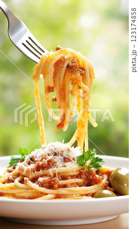 A fork lifts spaghetti Bolognese mid-air, with glistening sauce and falling Parmesan. Warm natural light and a sunlit window create a fresh, inviting Italian home-cooked atmosphere. 123174858