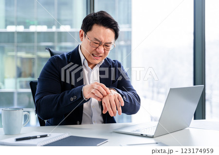 Stressed Korean Businessman Checking Time in Modern Office Setting Stressed Korean Businessman Checking Time in Modern Office Setting 123174959