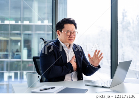 Asian Businessman Experiencing Stress at Workplace with Laptop and Coffee Mug Asian Businessman Experiencing Stress at Workplace with Laptop and Coffee Mug 123175136