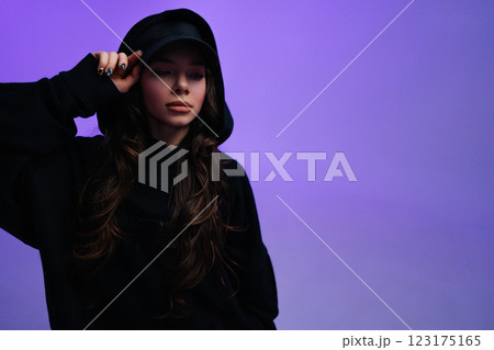 Young woman in black hoodie poses with confidence against purple backdrop 123175165