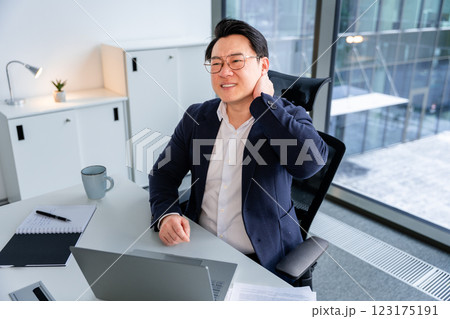 Asian Businessman Experiencing Neck Pain While Working in a Modern Office 123175191