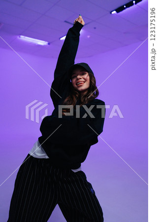 Individual enjoys dancing in a trendy outfit against a purple backdrop 123175196