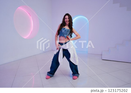 Young woman posing confidently in modern studio with colorful lighting 123175202
