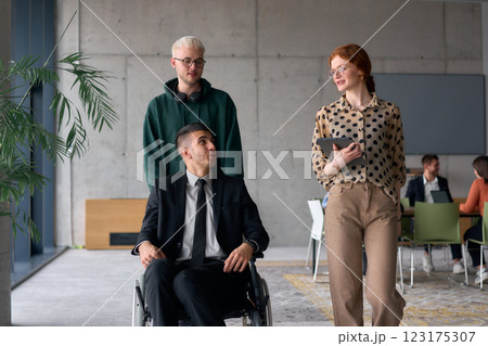 A diverse team of business colleagues, including a director in a wheelchair, engages in a collaborative discussion as they move together through a modern office space A diverse team of business colleagues, including a director in a wheelchair, engages in a collaborative discussion as they move together through a modern office space 123175307