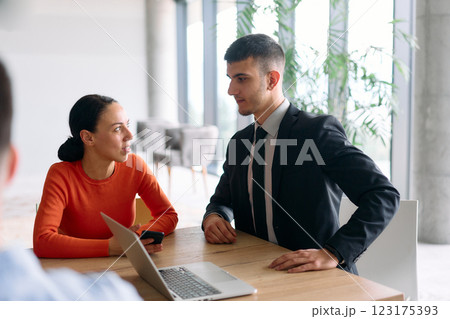 A young, diverse business team sitting together in a modern office, exchanging ideas and business plans, fostering collaboration and innovation for future success. 123175393