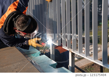 Industrial welder skillfully crafts a metal fence for a new business complex, using modern equipment that casts bright sparks and highlights the precision and dedication of the craft. Industrial welder skillfully crafts a metal fence for a new business complex, using modern equipment that casts bright sparks and highlights the precision and dedication of the craft. 123175404