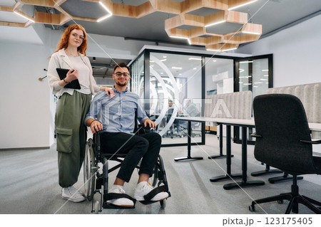 Business colleagues, collaborative business colleagues, including a person in a wheelchair, walk past a modern glass office corridor, illustrating diversity, teamwork and empowerment in the workplace. Business colleagues, collaborative business colleagues, including a person in a wheelchair, walk past a modern glass office corridor, illustrating diversity, teamwork and empowerment in the workplace. 123175405