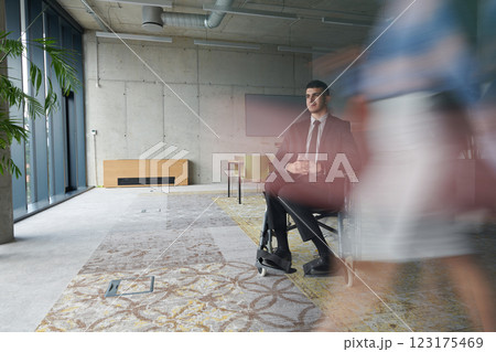 A businessman in a wheelchair navigating through a busy office, surrounded by his colleagues who are actively engaged in their work and collaboration A businessman in a wheelchair navigating through a busy office, surrounded by his colleagues who are actively engaged in their work and collaboration 123175469