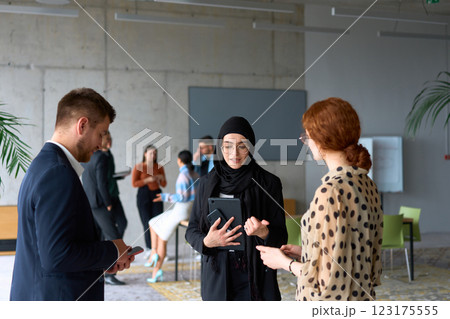 A diverse group of business professionals engages in a conversation during a work break in the office, with their colleagues visible in the background, fostering collaboration and connection A diverse group of business professionals engages in a conversation during a work break in the office, with their colleagues visible in the background, fostering collaboration and connection 123175555