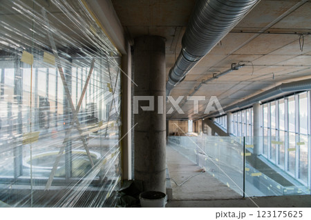 A captivating view of a modern business building under construction, showcasing its raw industrial interior with exposed steel beams and concrete walls bathed in the warm, golden hues of a sunset 123175625