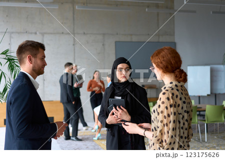 A diverse group of business professionals engages in a conversation during a work break in the office, with their colleagues visible in the background, fostering collaboration and connection A diverse group of business professionals engages in a conversation during a work break in the office, with their colleagues visible in the background, fostering collaboration and connection 123175626
