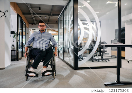 In a large modern corporation, a determined businessman in a wheelchair navigates through a hallway, embodying empowerment and inclusivity in the corporate world. In a large modern corporation, a determined businessman in a wheelchair navigates through a hallway, embodying empowerment and inclusivity in the corporate world. 123175808