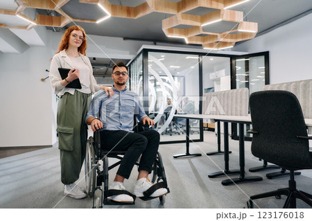 Business colleagues, collaborative business colleagues, including a person in a wheelchair, walk past a modern glass office corridor, illustrating diversity, teamwork and empowerment in the workplace. Business colleagues, collaborative business colleagues, including a person in a wheelchair, walk past a modern glass office corridor, illustrating diversity, teamwork and empowerment in the workplace. 123176018