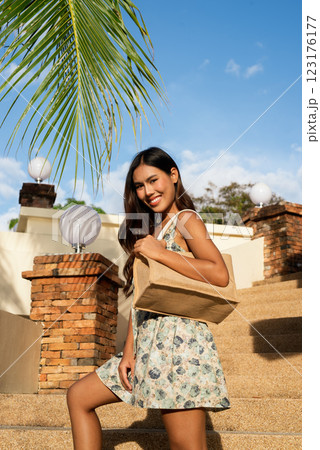 Young Asian woman holding bag outdoors during summer Young Asian woman holding bag outdoors during summer 123176177