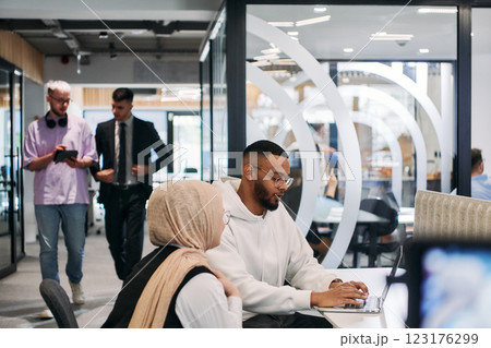 In a modern office setting, an African American businessman and his Muslim colleague, wearing a hijab, engage in collaborative discussions, tackling various business tasks and solving problems In a modern office setting, an African American businessman and his Muslim colleague, wearing a hijab, engage in collaborative discussions, tackling various business tasks and solving problems 123176299