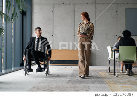 Director in a Wheelchair Navigating the Office While Discussing Business Challenges with a Colleague 123176387