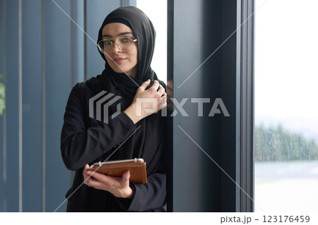 A stunning Muslim businesswoman is captured in a close up portrait, holding a tablet in her hands, showcasing her captivating green eyes behind stylish prescription glasses, radiating elegance A stunning Muslim businesswoman is captured in a close up portrait, holding a tablet in her hands, showcasing her captivating green eyes behind stylish prescription glasses, radiating elegance 123176459