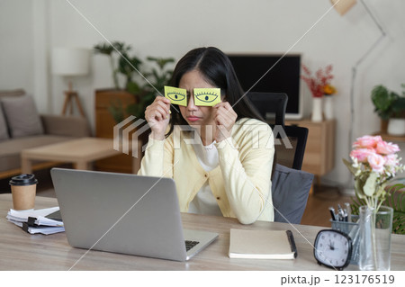 Woman in home office using sticky notes to stay awake while working on a laptop, showcasing remote work challenges. Woman in home office using sticky notes to stay awake while working on a laptop, showcasing remote work challenges. 123176519