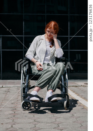 In front of a modern corporate building, a young woman sitting in a wheelchair confidently, symbolizing empowerment, inclusivity, and the strength to overcome challenges in the business world 123176636