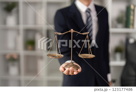 Young Asian lawyer presenting legal scales in office, symbolizing justice and balance in law practice. 123177486