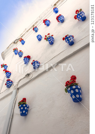 Cordoba town in Spain. Vibrant red flowers in blue polka-dot pots adorn a whitewashed wall, creating a cheerful and picturesque scene. Cordoba town in Spain. Vibrant red flowers in blue polka-dot pots adorn a whitewashed wall, creating a cheerful and picturesque scene. 123178181