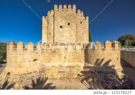 The Calahorra Tower on a one side of the Roman Bridge in Cordoba town in Spain. Ancient stone tower and walls under a bright blue sky. A historical landmark, possibly a castle or fortress. The Calahorra Tower on a one side of the Roman Bridge in Cordoba town in Spain. Ancient stone tower and walls under a bright blue sky. A historical landmark, possibly a castle or fortress. 123178227