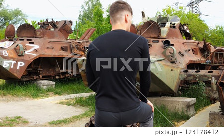 Young man looking at destroyed military equipment of the russian army. Exhibition of rusty and burned-out armored vehicles on ukrainian territory. War between Ukraine and russia. Slow motion 123178412