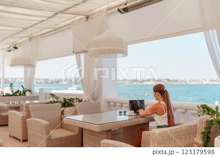 Woman coffee cafe laptop sea. Female freelancer using laptop on coffee break in modern cafe with sea view in the morning 123179598