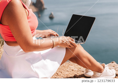 A woman is sitting on a rock by the water with a laptop open in front of her. She is typing on the laptop and she is focused on her work. Concept of productivity and concentration. A woman is sitting on a rock by the water with a laptop open in front of her. She is typing on the laptop and she is focused on her work. Concept of productivity and concentration. 123179633