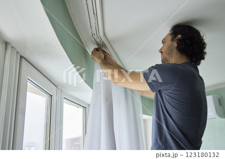 A person is actively hanging beautiful curtains in a bright and cheerful room space 123180132