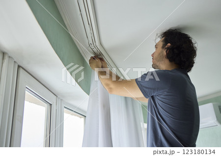 A person is actively hanging beautiful curtains in a bright and cheerful room space 123180134