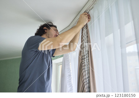 A person is actively hanging beautiful curtains in a bright and cheerful room space 123180150
