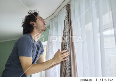 A person is actively hanging beautiful curtains in a bright and cheerful room space 123180152