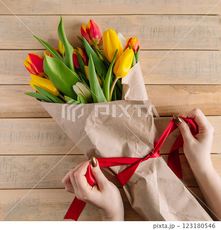 Woman florist ties red bow on large bouquet of colorful tulips. Fresh spring flowers 123180546